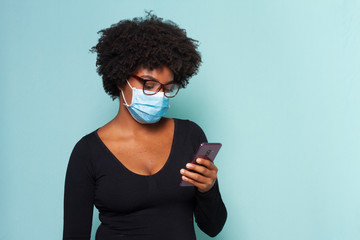 black woman with black power hair wearing protective mask with smartphone in hands and wearing...