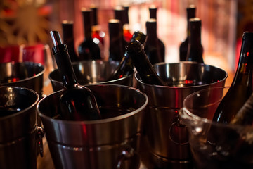 several black bottles of wine stand in chrome metal buckets filled with ice well lit by a soft light against the soft red light of the establishment