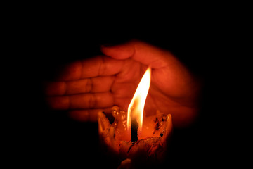 Hand protecting candle light from the wind in darkness on black background