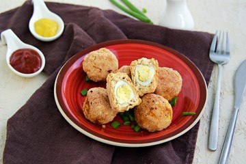 Scottish eggs, boiled quail eggs in minced chicken on a red clay plate on a light concrete background. Can be served as a starter or main course. Recipes with eggs.