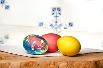 Three eggs on a white napkin, on a wooden board on a table, behind a blurred white background with a blue pattern