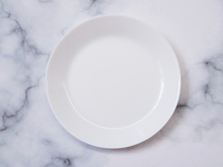 Top view of white glazed ceramic round dish for food isolated on marble table.