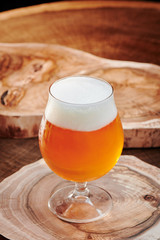 Light beer with foam in a round beer glass (snifter) on a leg on a wooden background. Close up. 
