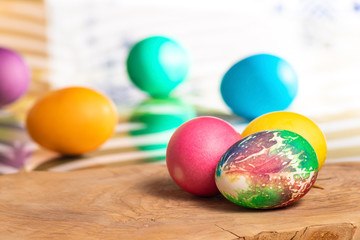 Three eggs in the lower right corner on a wooden board, in the background a blurred background with colored eggs