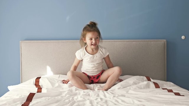 Playful little girl having fun jumping on bed.