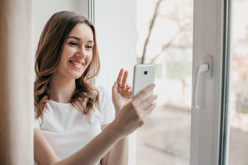 A young woman holds a mobile phone in her hands and communicates by video call with her friends, family, employees, parents, coronavirus, quarantine, isolation, stay home