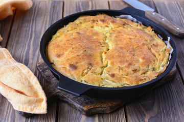 Freshly baked pie ready for dinner, hot pie stuffed in a cast iron pan on a wooden board next to napkin and knife