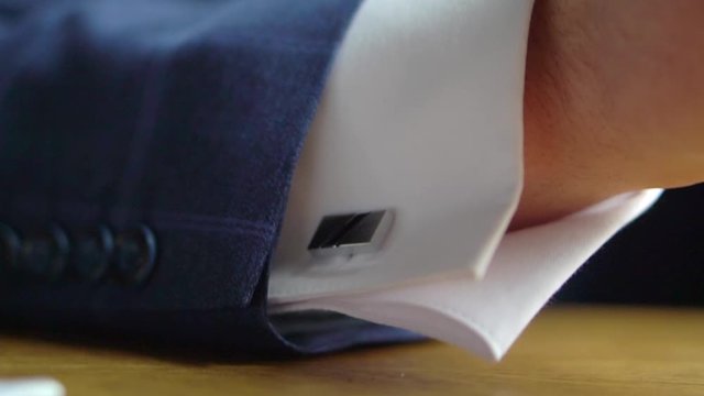 A man's cufflink on the shirt under the blue jacket on the groom's hand