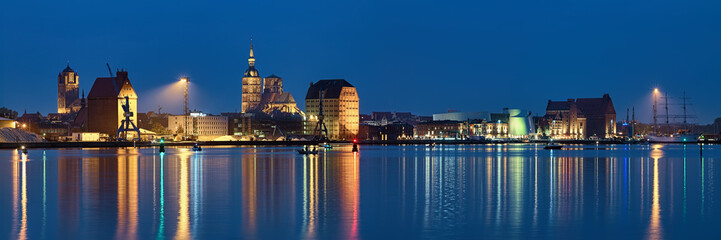 Fototapeta na wymiar Stralsund, Germany. Panoramic view of the North Harbor in dusk with St. James Church (left), St. Nicholas Church (center), historical warehouses (right).