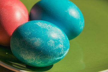 Easter photo from Russia. Chicken eggs are painted in blue and pink according to ancient tradition, lie on a green ceramic plate. Retro style still life in the spring sunshine.