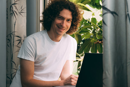 A Young Man Near The Window With A Laptop Rejoices At The End Of Quarantine From The Coronavirus. He Is Tired Of Working From Home And Is Looking Forward To A Future Life After The Epidemic.