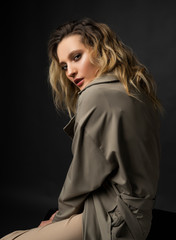 Beautiful girl wearing a casual trendy trousers, turtleneck and raincoat posing on a dark background. Fashionable, advertising, lifestyle and commercial design.