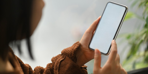 Cropped image of beautiful woman on brown cotton sweater holding a white blank screen smartphone in...