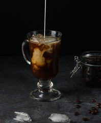 The cream is poured into a glass of iced coffee. Making a coffee latte, filmed in a low key.