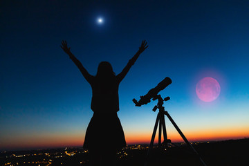 Silhouette of a woman and telescope with twilight sky.