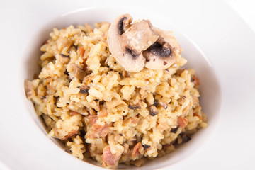Risotto with button mushroom and bacon decorated with mushroom on a plate on a white background