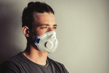 Young man in a modern medical mask in a gray t-shirt on a light background, during a home quarantine of the coronavirus infection epidemic. Stay home concept. Stop panic. Portrait with copy space