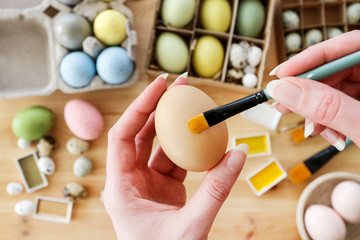 Woman holds an Easter egg and a brush in her hand.