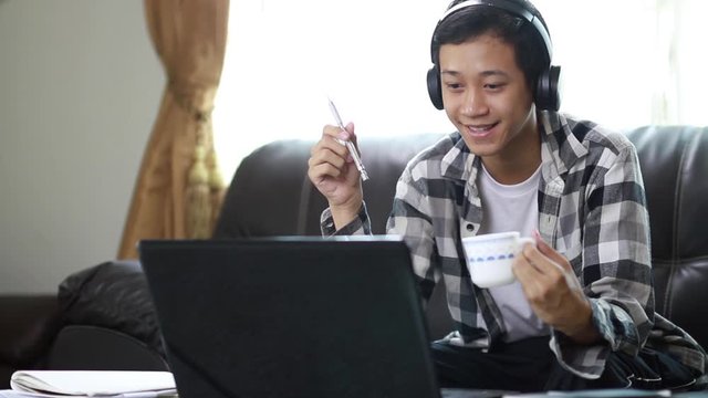 Happy teenager men wearing a headset while having fun with online class through a laptop computer at home Living room.