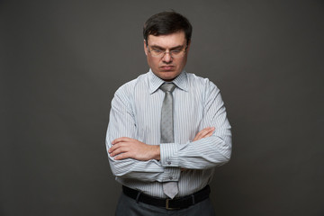 a man looking down, dressed as a businessman posing in a studio on a gray background, glasses, a light striped shirt and tie - casual office wear