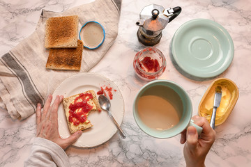 Female hands with milk and coffee cup and toast with butter and marmalade. From above.