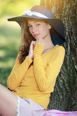 Jeune femme avec un chapeau de paille bleu souriante au pied d'un arbre