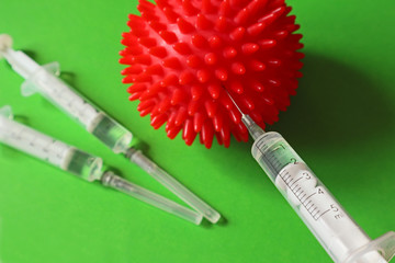 Syringe and red Coronavirus on a green background. Injection of a cure for the virus COVID-19....