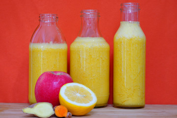 Glass bottles filled with colorful fresh homemade apple, lemon and ginger smoothies