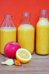 Fototapeta na wymiar Glass bottles filled with colorful fresh homemade apple, lemon and ginger smoothies