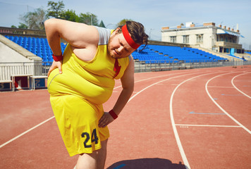 A fat man holds his back in the stadium.