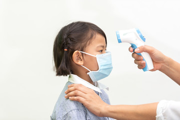 Pediatrician or doctor checks elementary age girl's body temperature using infrared forehead...
