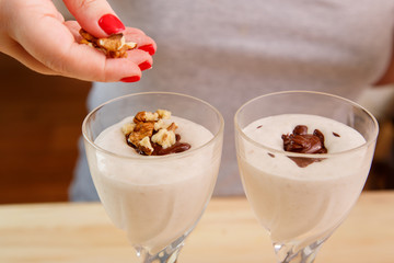 A female hand sprinkles a crushed nut with a smoothie of banana and ice cream with chocolate.