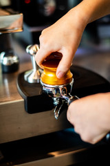 A man's hand holds a wooden handle that compresses golden coffee, pressing the coffee powder in the coffee stem.