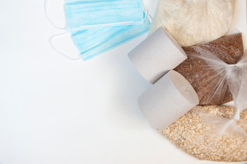 Food donation on a white background. Buckwheat, rice, oatmeal in plastic bags, toilet paper and medical masks. Top view with copy space.