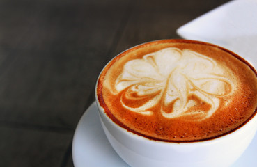 Hot latte art coffee in white cup on white plate with copy space on left. Close up and selective focus at corner of cup. Refreshment drinking