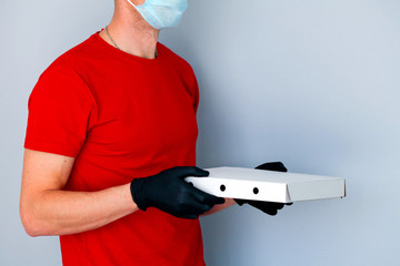 A man hands rubber gloves with a box pizza . Food delivery during the quarantine of the coronavirus pandemic.