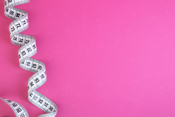 Unfolded white tape measure, White measuring tape isolated on pink background. Close the tailor measuring tape on a pink background. The concept of sports, diet, fitness, healthy eating. Copy space
