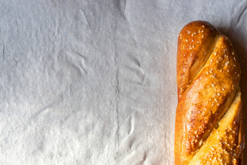 Fresh baguette with sesame seeds on gray wrapping paper.