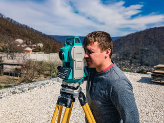 Surveyor with a total station at work. A set of a total station and a surveyor taking measurements at a construction site against the backdrop of mountains and a blue sky. Construction work on a sunny