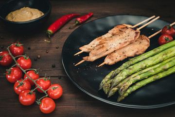 Plate with grilled chicken skewers, green asparagus and peanut sauce on dark wood