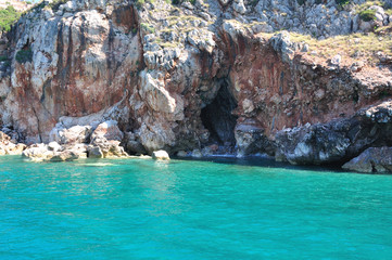 Obraz premium Clear turquoise sea and rocks on the shore. In the rock, the entrance to the cave.