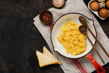 Scrambled eggs for breakfast on frying pan, dark wooden table background. Traditional English breakfast.Top view with cope space.