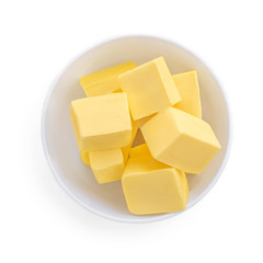Butter pieces in bowl isolated on white background, top view. Fresh butter chunks  close up.