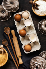 White and yellow chicken eggs and shells in an old cellulose vintage container with flour, sugar, wooden spoons and rolling pin on old dark wooden background. Baking and culinary background. Top view 