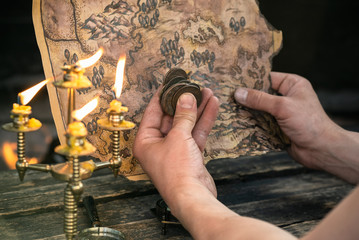 Pirate is looking on the treasure map and ancient coins in his hands close up on burning fire...