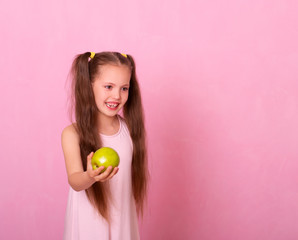 Smiling Girl Holding Apple Looking At Camera Standing On pink Background.