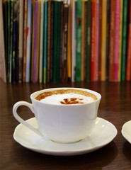 Cup of Cappuccino Coffee with Blurry Rows of Books in the Backdrop