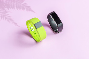 Activity smart trackers on light pink background. Black and green fitness health watch with fern shadow, sport bracelets