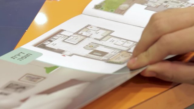 Israeli man looking at real estate information brochure. Close up on his hand. The hebrew words Dirot Hupa" (canopy apartments) are appears. Also the number of rooms and its size appears.