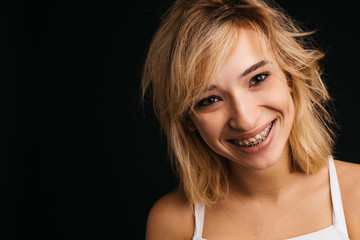 Young blonde cheerful woman stand on right side and smile. Posing on camera with positive mood. Sexy girl in white shirt isolated over black background.